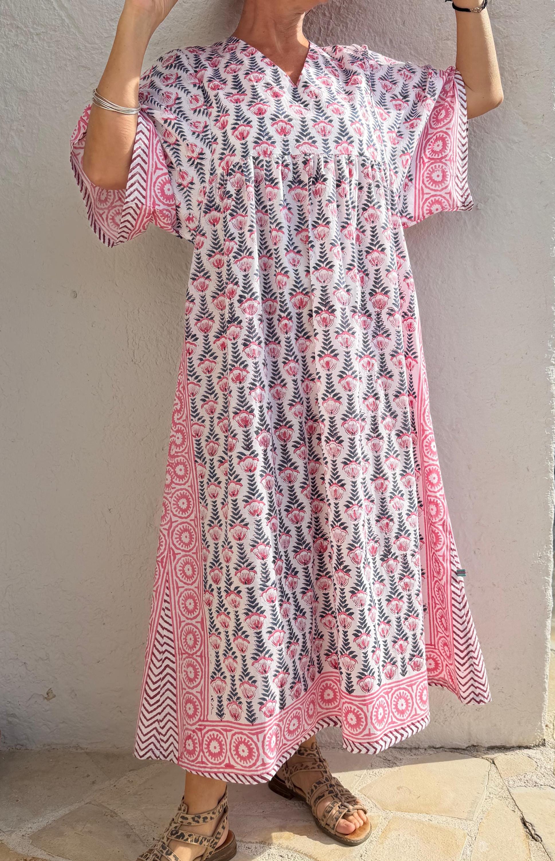 Peut inclure: Longue robe à imprimé floral blanc et rose avec manches courtes. La robe présente un col en V et une silhouette ample et fluide. Les manches et l'ourlet sont bordés d'une bordure géométrique rose. La robe est en tissu léger, idéale pour l'été.