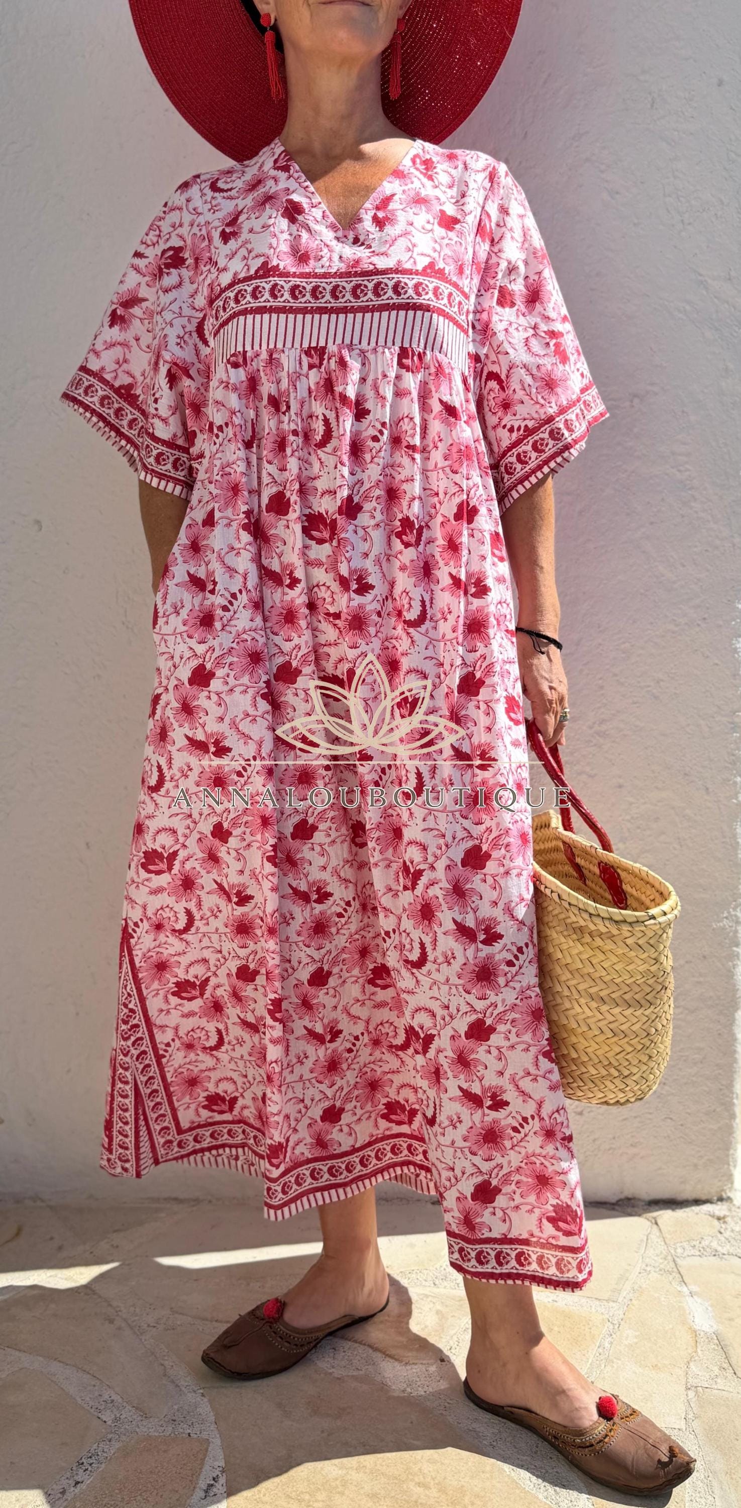 Peut inclure: Une robe midi ample à motif floral rouge sur fond blanc, dotée de manches courtes et d'un col en V. Le vêtement présente une bande rayée horizontale sur la poitrine et l'ourlet, avec le texte ANNALOUBOUTIQUE et un logo en forme de lotus.