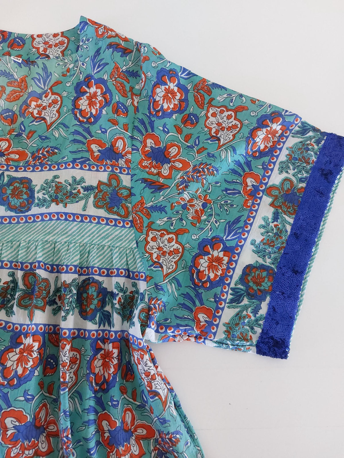 Détail du tissu et des finitions : robe ample turquoise et orange, sequins bleus